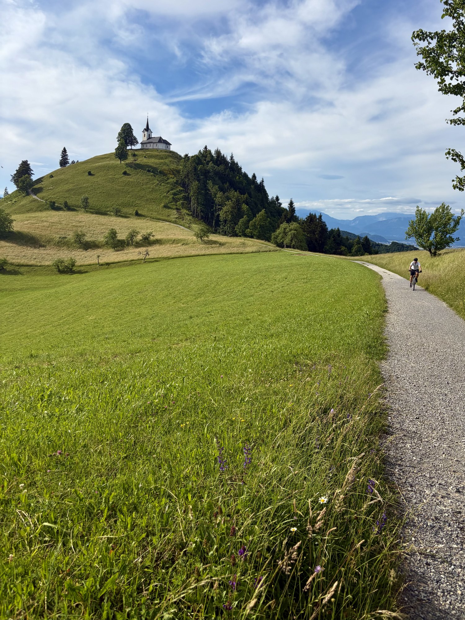 Gravel cyclist riding a path below the hilltop church of St Jakob above the Ljubljana basin