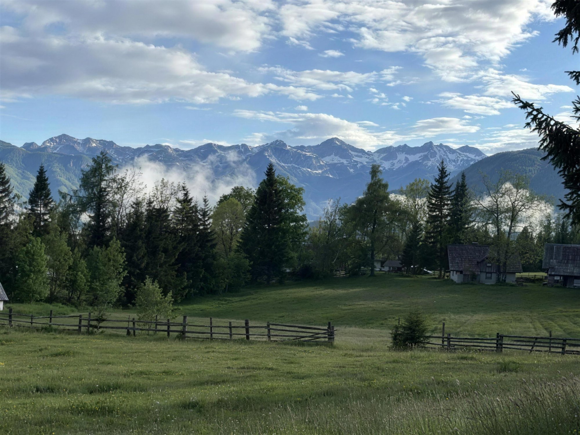 A fenced alpine meadow in the morning with the snow-dusted ridgeline of the Julian Alps behind